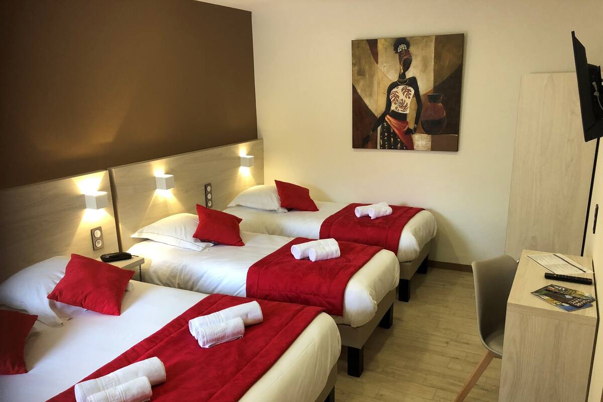 Habitación de hotel con tres camas, cada una con ropa de cama roja y blanca, y un cuadro en la pared.