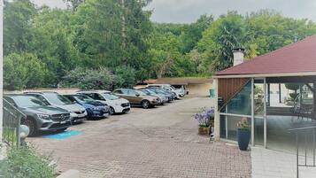 A parking lot with several cars, a building with a red roof, and a view of a forested area in the background.