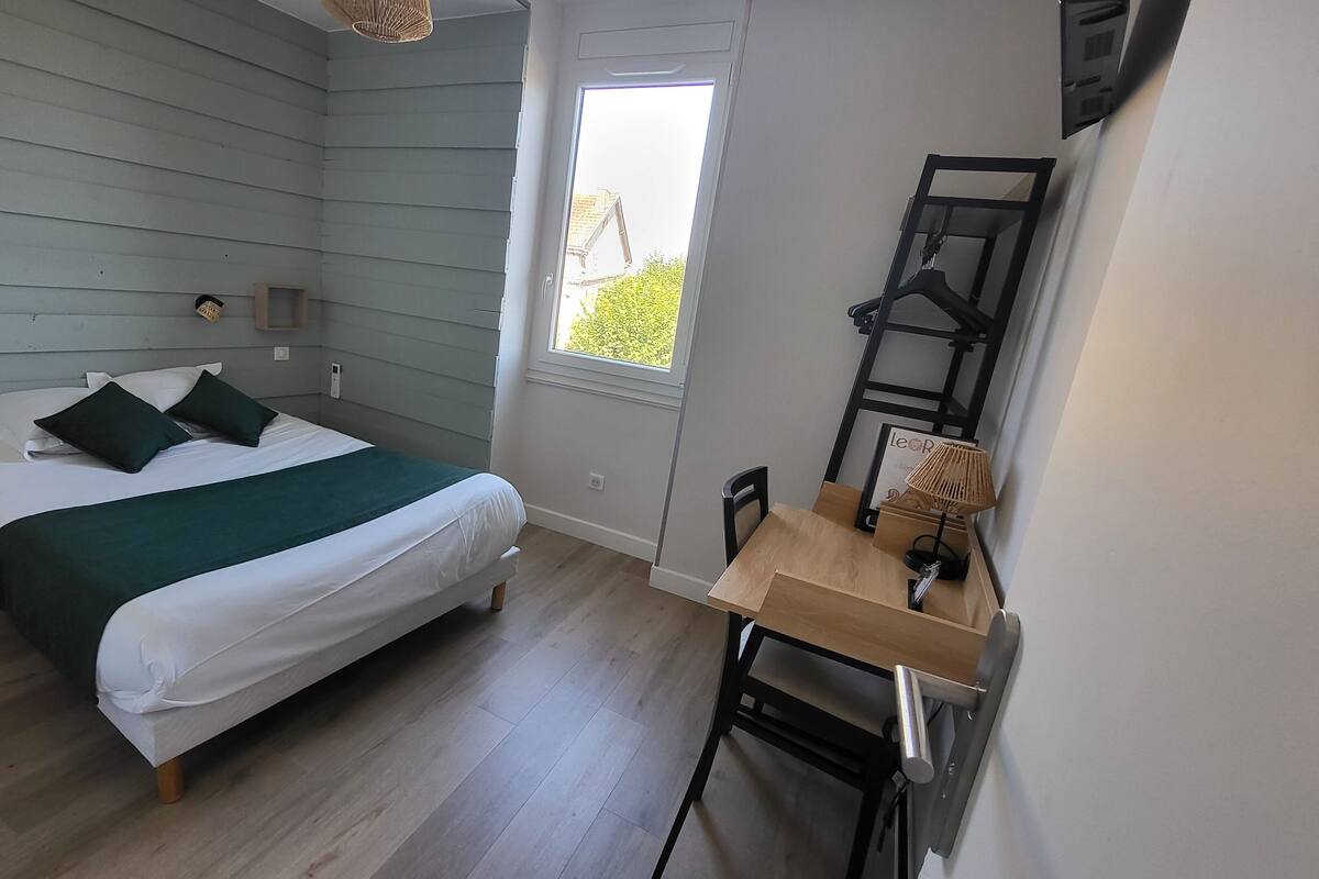 Un dormitorio con cama, escritorio, silla, ventana y lámpara colgante.