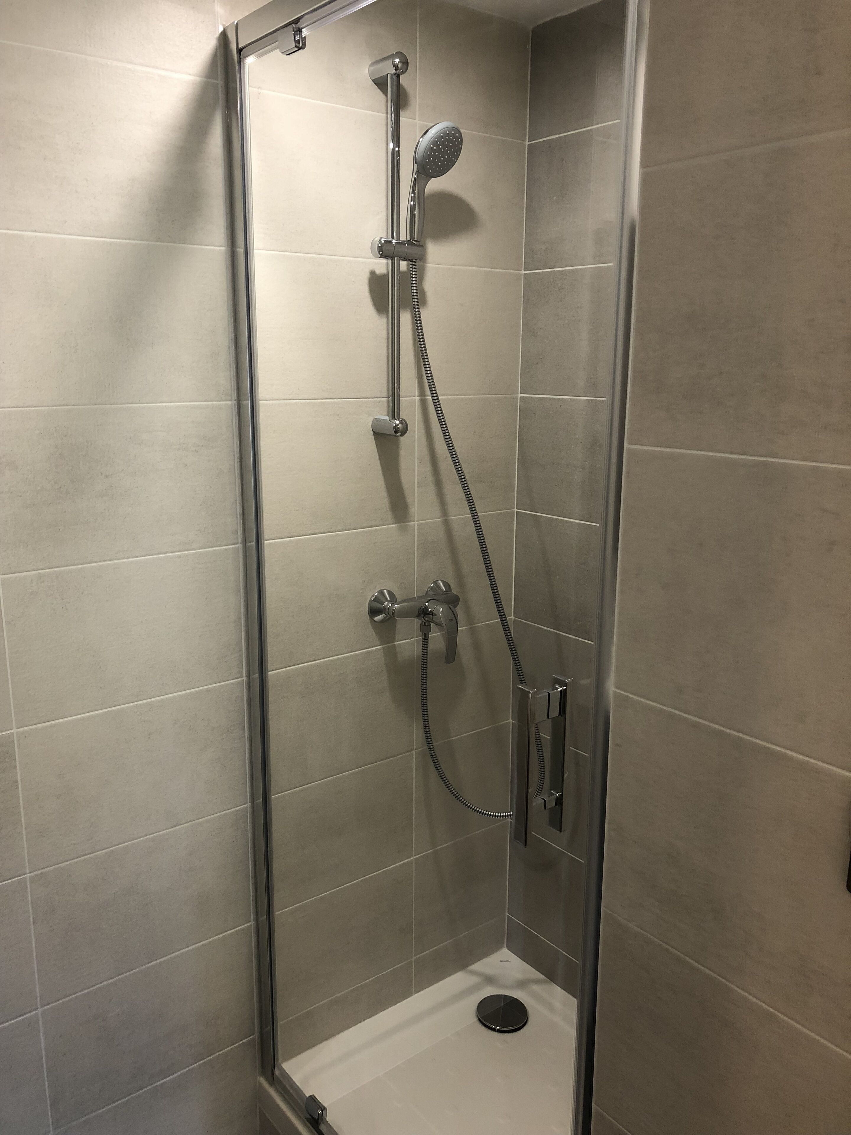 Un box de ducha con paredes de vidrio, un cabezal de ducha de mano, un grifo empotrado y un panel de control.