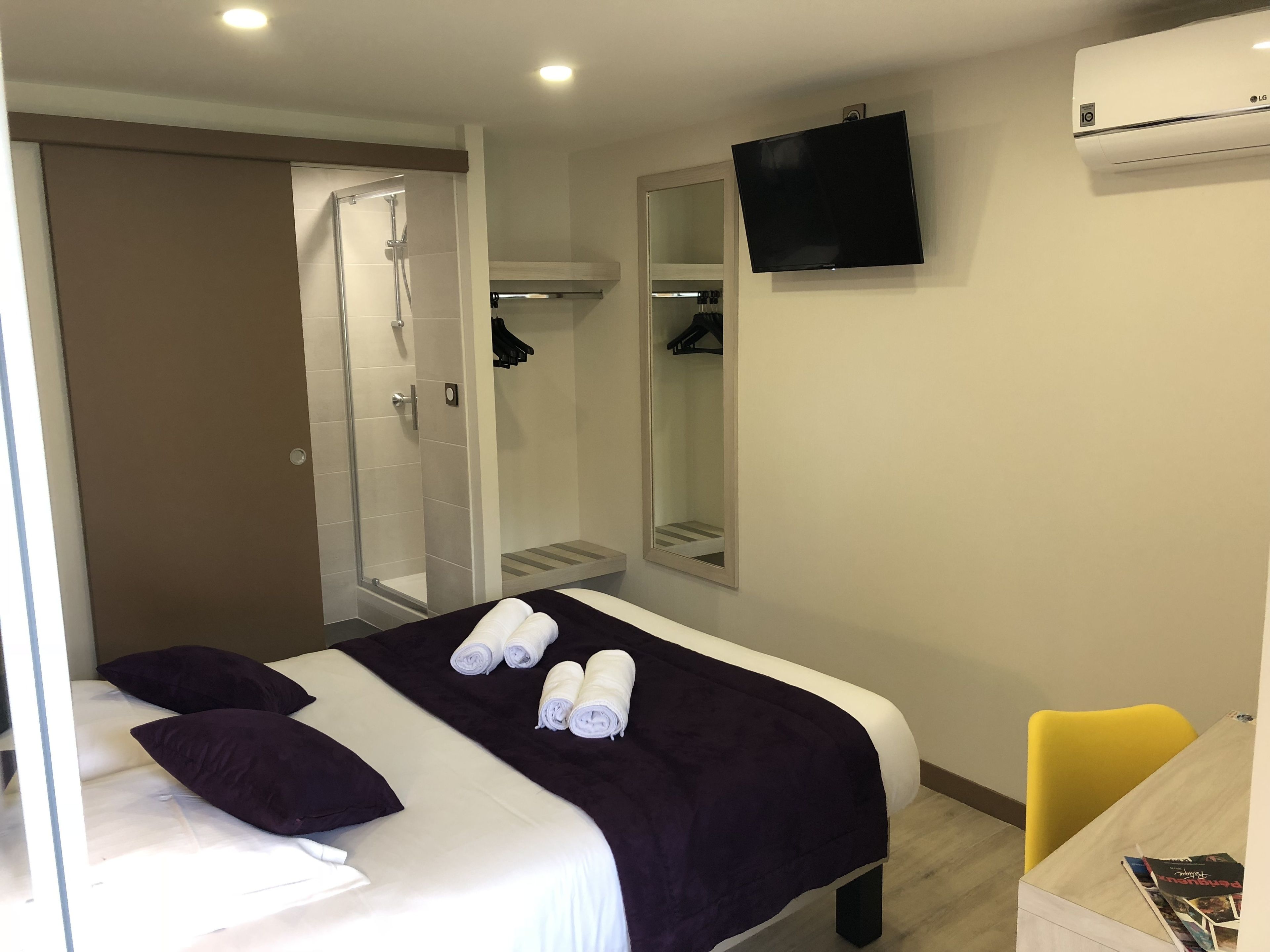 Una habitación de hotel con cama, ducha, televisión y escritorio con silla.