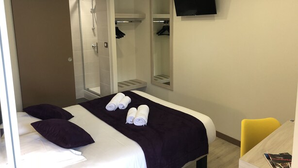 Een hotelkamer met een bed, douche, televisie en bureau met stoel.