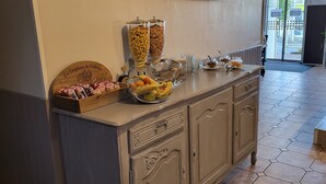 A buffet area with a variety of food items, including fruits and pastries, and a wooden sign with a logo. - Hôtel Le RELAX (Boulazac-Isle-Manoire)