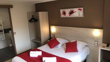 Habitació d'hotel amb llit, roba de llit vermella i blanca, un capçal de llit de fusta, un quadre de flors, una taula de nit amb un telèfon i una làmpada, i un penjador de tovalloles.