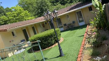 Un bâtiment jaune avec un toit recouvert de tuiles, un petit patio avec des chaises et un jardin bien entretenu.
