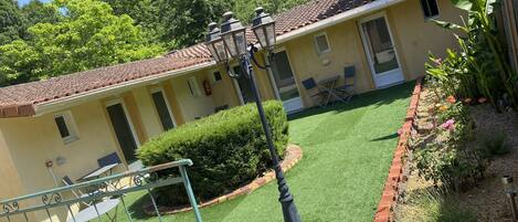 A yellow building with a tiled roof, a small patio with chairs, and a well-maintained garden.