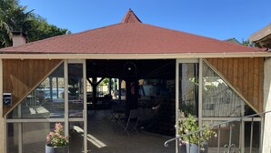 A covered outdoor seating area with a tiled roof, glass walls, and potted plants. - Hôtel Le RELAX (Boulazac-Isle-Manoire)