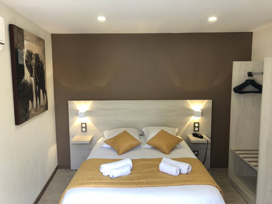 A hotel room with a large bed, two bedside tables, a nightstand, a painting on the wall, and a wooden wardrobe.