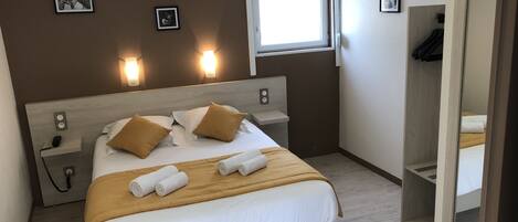 A hotel room with a bed, bedside tables, a nightstand, a window, and wall-mounted lights.