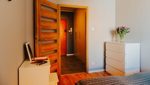 A bedroom with a wooden wardrobe, a bedside table with a book, a white dresser, and a vase of flowers. - Elite Apartments Seaview Horyzont (Gdansk)