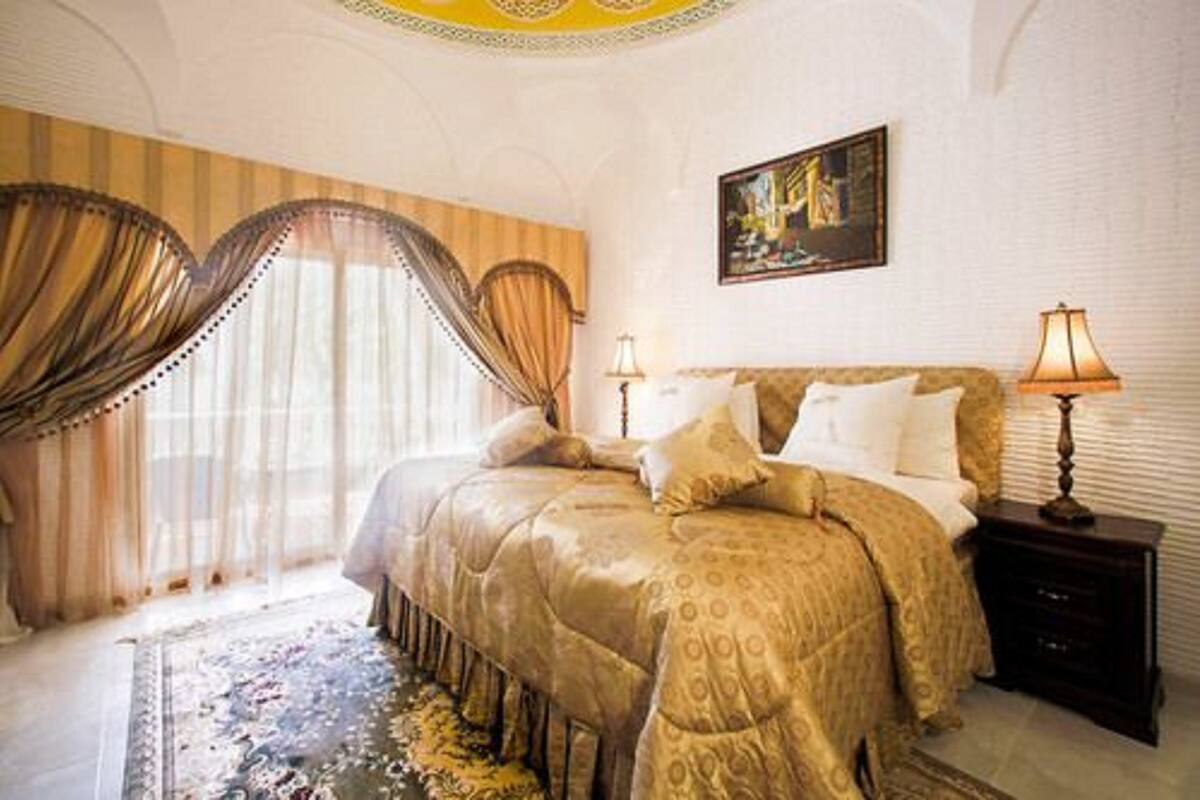 Un dormitorio con una cama grande, dos lámparas de noche, una obra de arte enmarcada en la pared y una alfombra estampada.