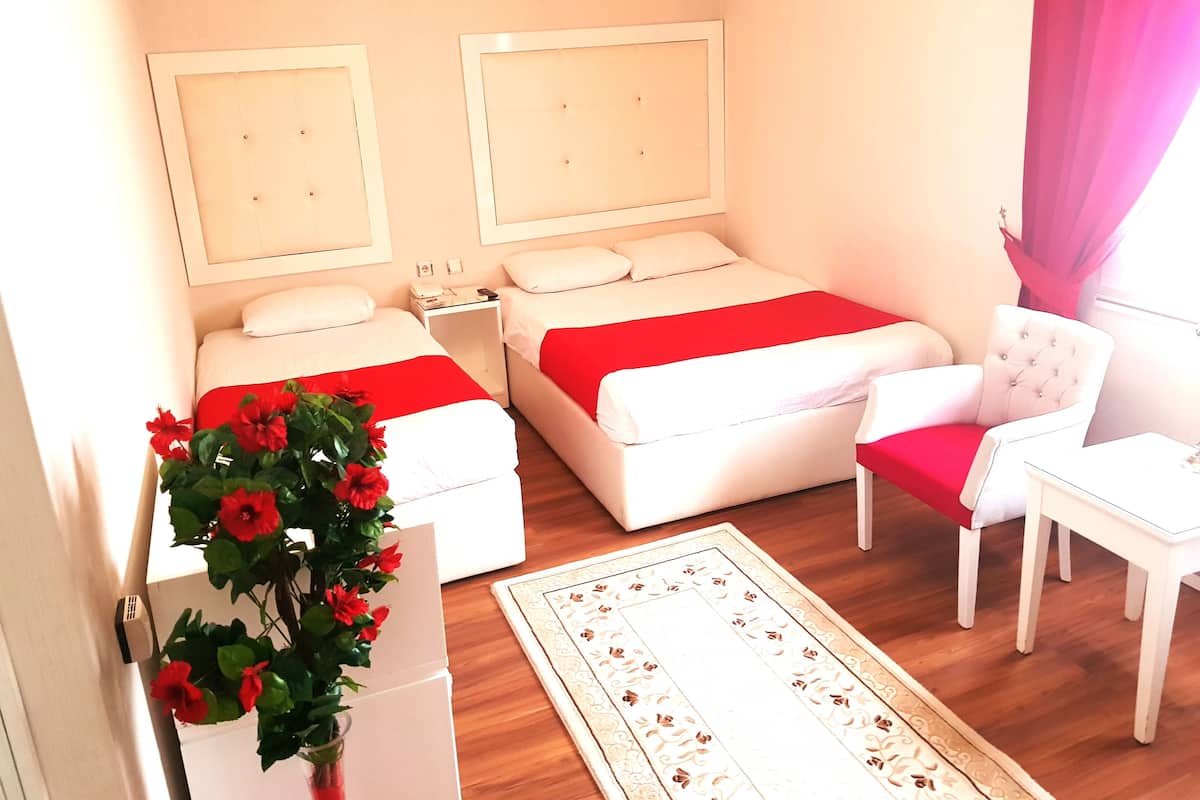 A hotel room with two beds, a chair, a small table, a nightstand, and a red flower arrangement.