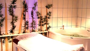A spa room with a massage table, a bathtub, and bamboo plants. - Business Park Hotel (Ankara)