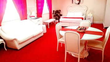 A hotel room with a red carpet, white furniture, a round dining table, and a bed with a white headboard.