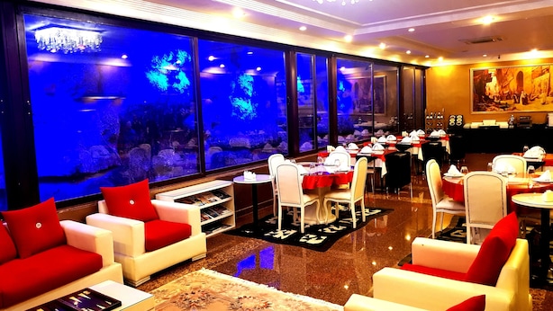 A restaurant with a large aquarium, white and red seating, and a chandelier. - Business Park Hotel (Ankara)