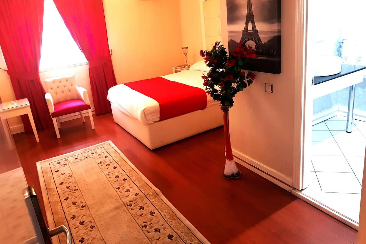 A hotel room with a bed, a chair, a vase with flowers, and a painting of the Eiffel Tower.