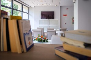 Een receptiebalie met stoelen, een televisie en een raam met zonwering.