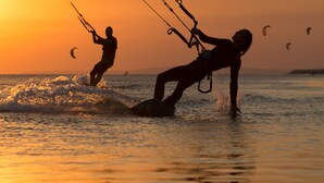 Escena de playa con dos personas practicando windsurf durante el atardecer.