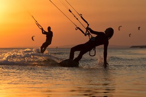 Une scène de plage où l’on voit deux personnes faire de la planche à voile au coucher du soleil.