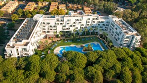 Un hotel moderno con piscina central, varios balcones y un jardín en la azotea.
