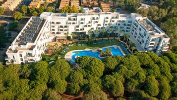 Un hotel moderno con piscina central, varios balcones y un jardín en la azotea.