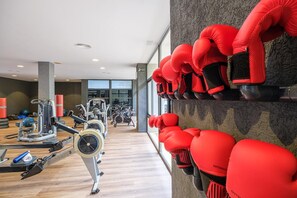 Een sportschool met diverse trainingsapparaten, waaronder loopbanden en krachttoestellen, en rode bokshandschoenen die aan de muur hangen.