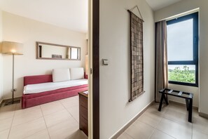 A modern hotel room with a red sofa, a small wooden table, a large window with a view, and a wall-mounted mirror. - Estival Isla Cristina (Isla Cristina)