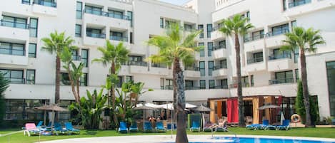 A modern hotel with a swimming pool surrounded by palm trees and lounge chairs.