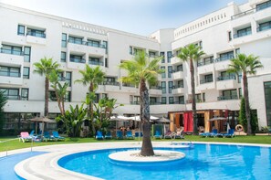 Un hotel moderno con piscina rodeada de palmeras y sillas de descanso.