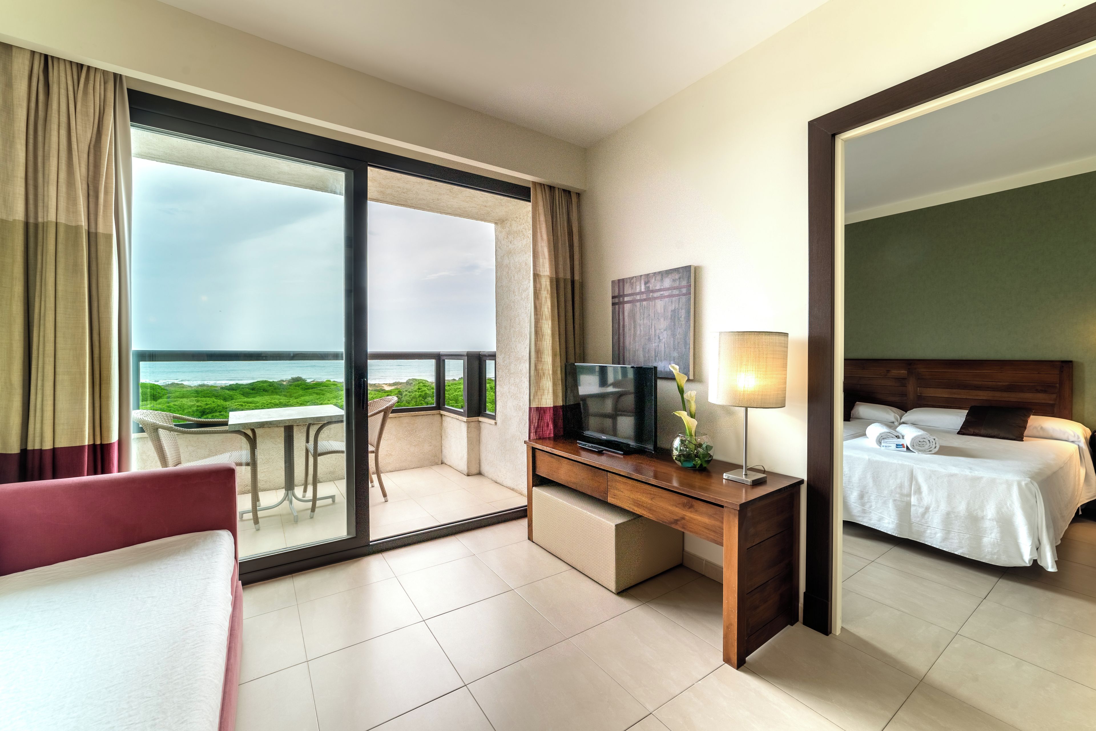 Habitación de hotel con balcón, cama, escritorio con televisor y vista al mar.
