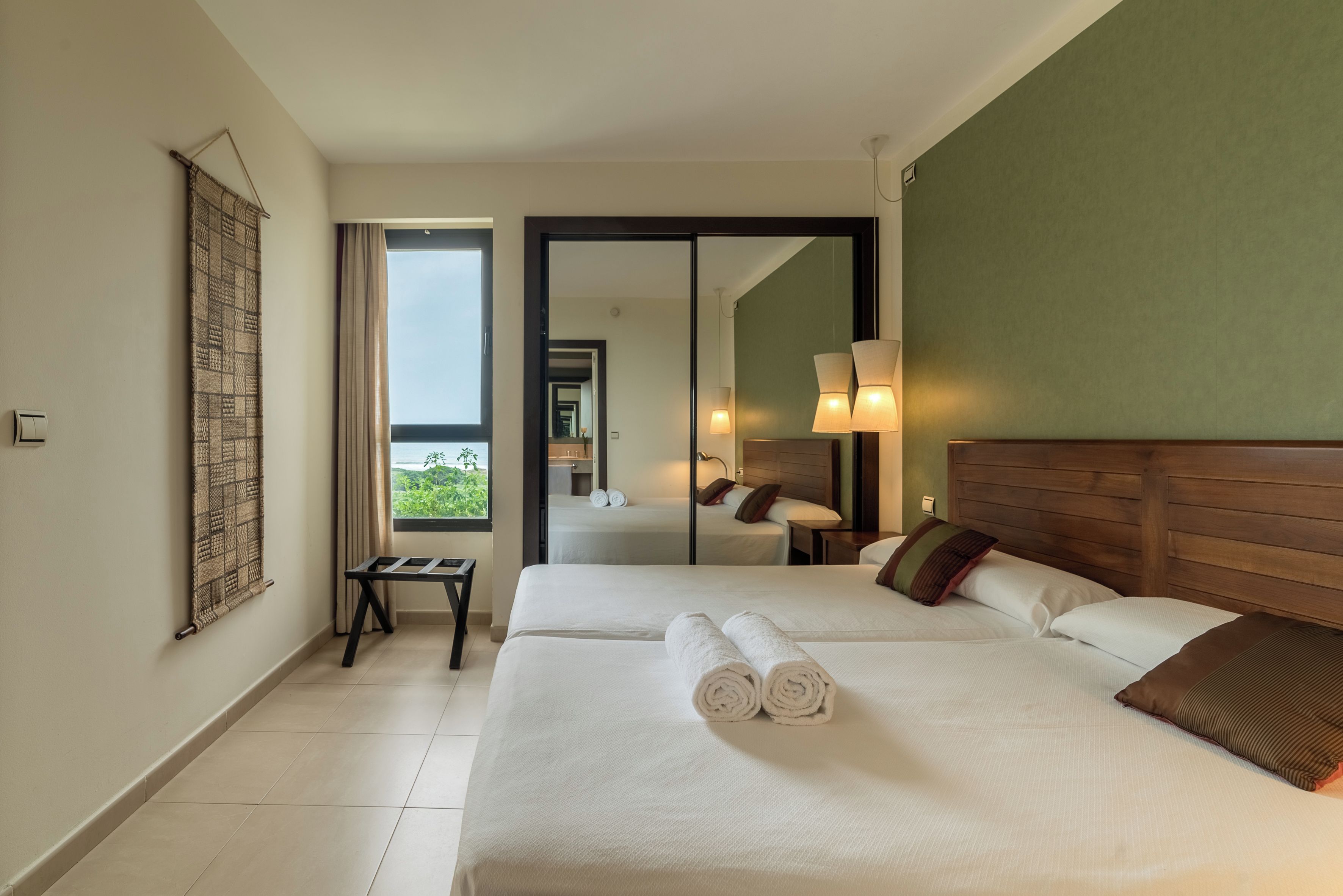 Habitación de hotel con dos camas, vistas al exterior, un espejo y una mesita.