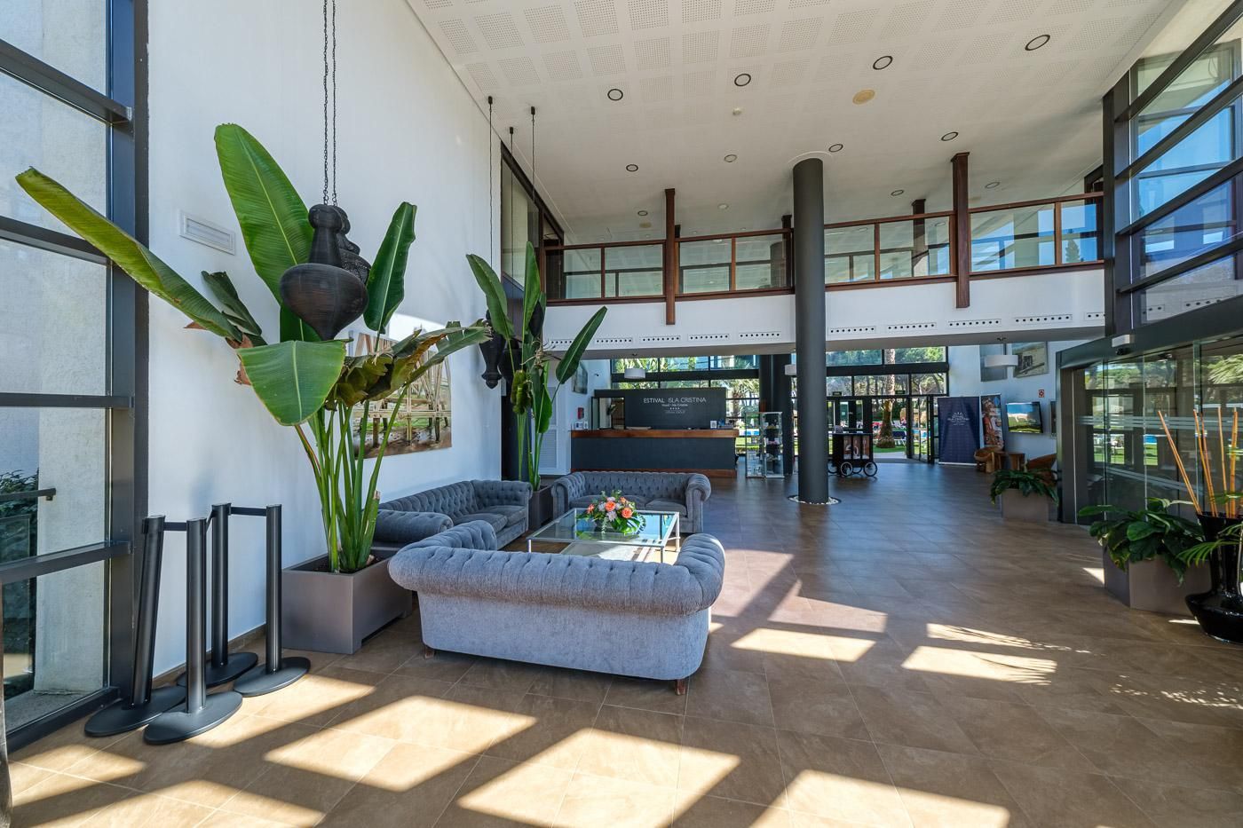 Un hall espacioso con diseño moderno, que cuenta con una zona de estar con sofás y una mesa de centro, ventanas amplias que dejan entrar luz natural y un mostrador de recepción.