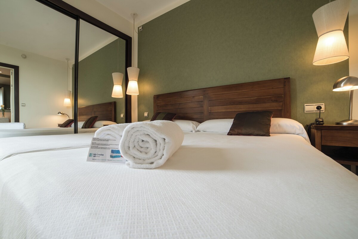 Een hotelkamer met een groot bed, een houten hoofdbord, een spiegel en twee bedlampjes.