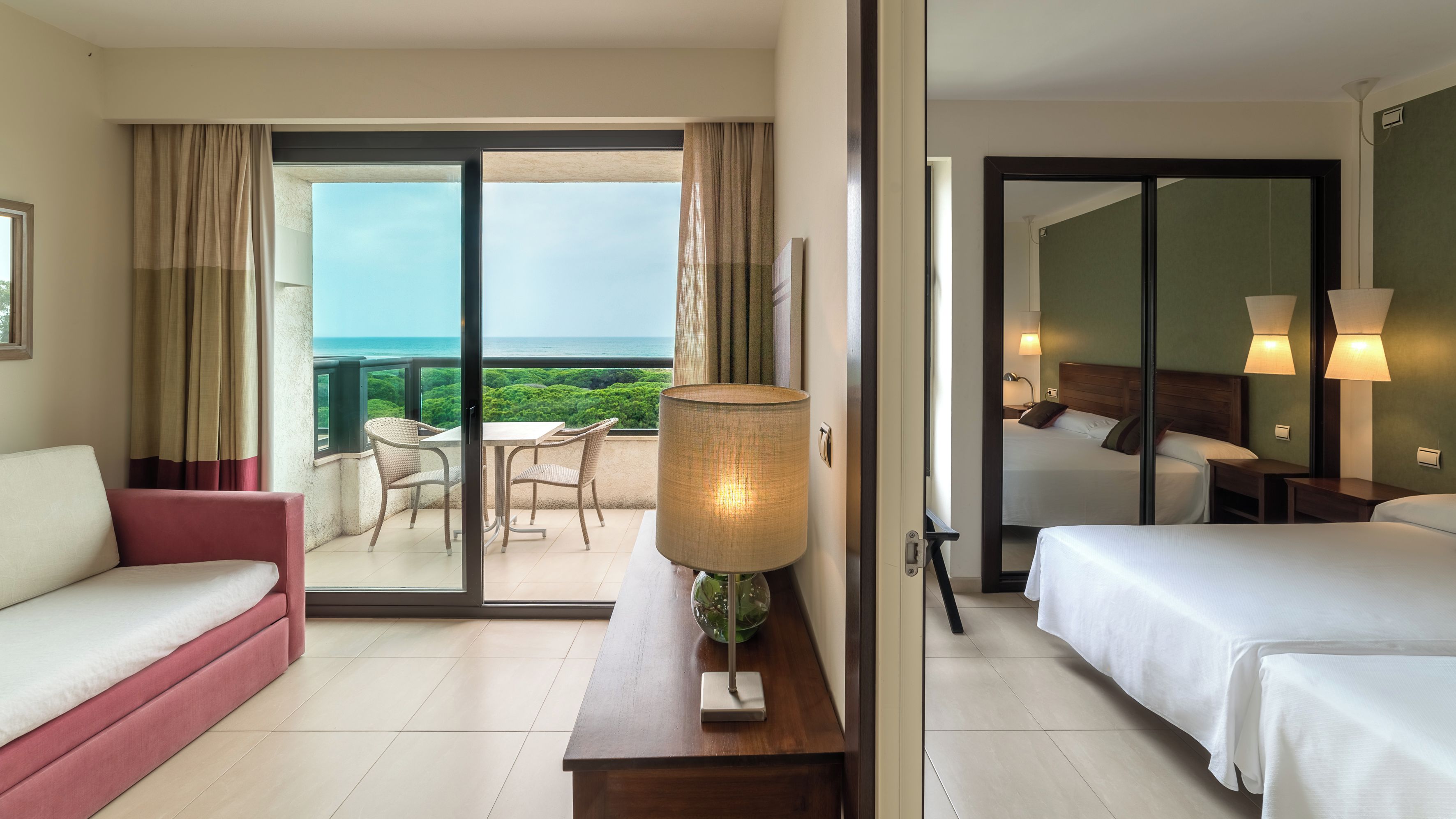 Habitación de hotel con balcón, cama, sofá y una mesa con lámpara.
