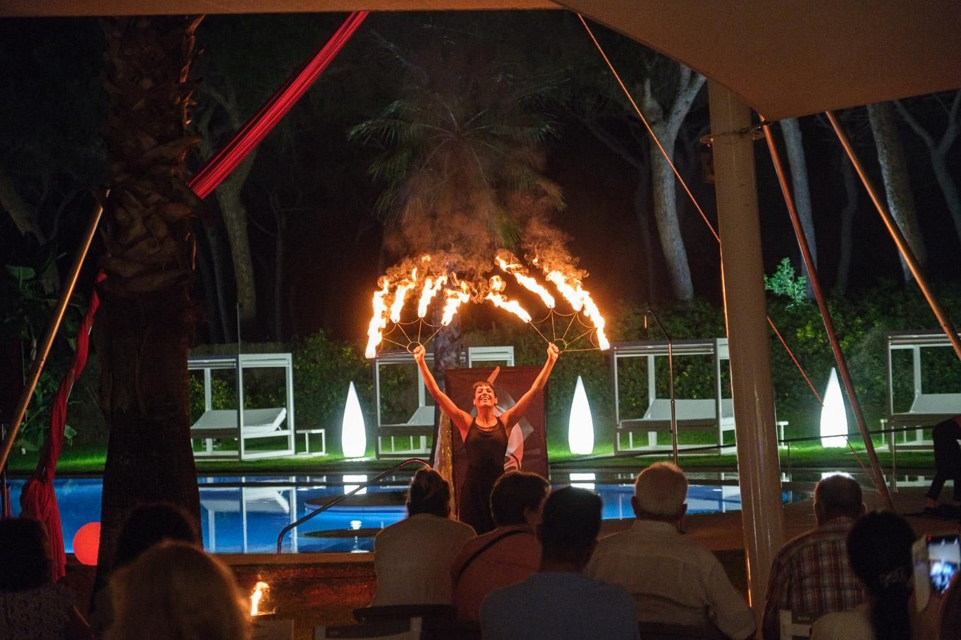 Una persona realizando trucos de fuego en un entorno exterior con piscina y palmeras.