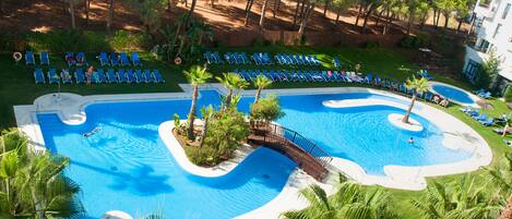 Een resort met een groot zwembad, ligbedden en palmbomen.