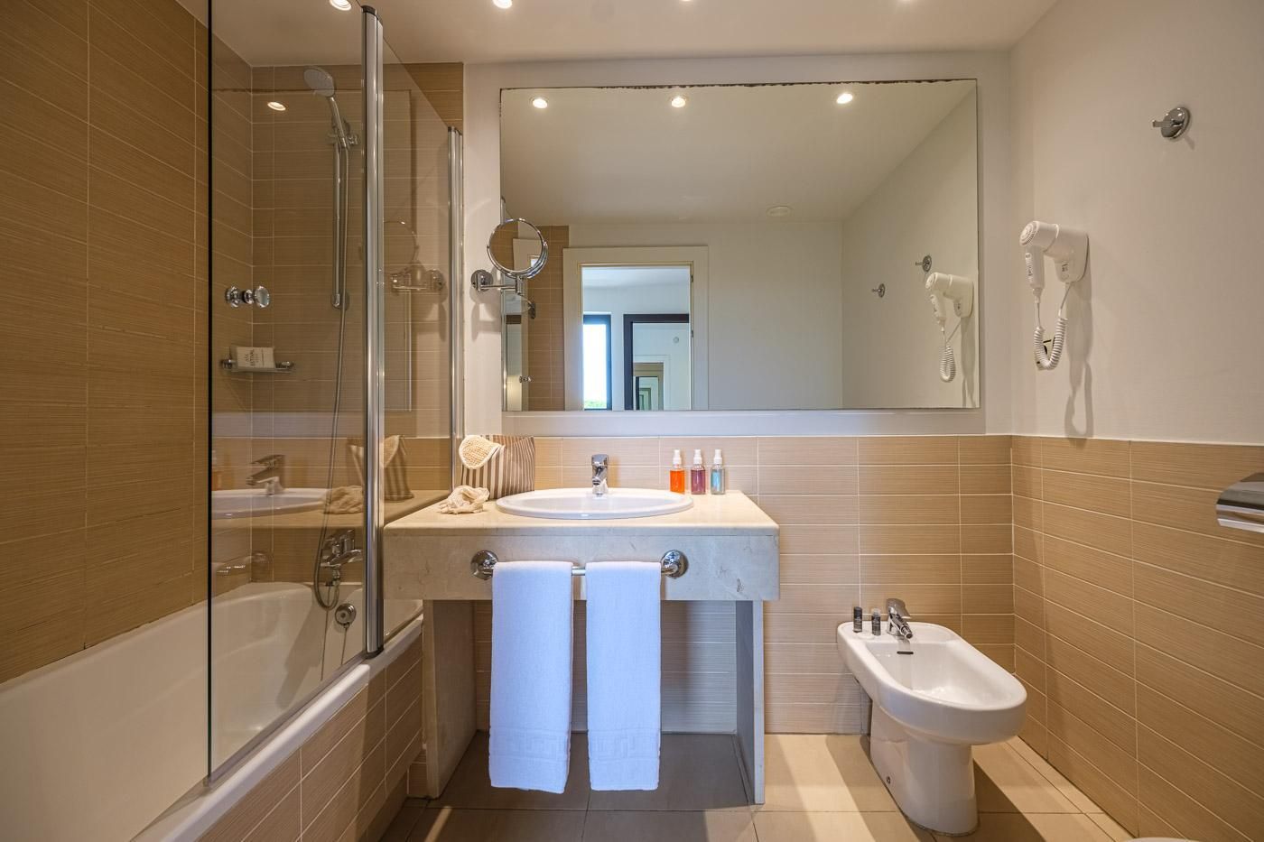 A modern bathroom with a glass-enclosed shower, a sink with a mirror, a bidet, and a toilet.