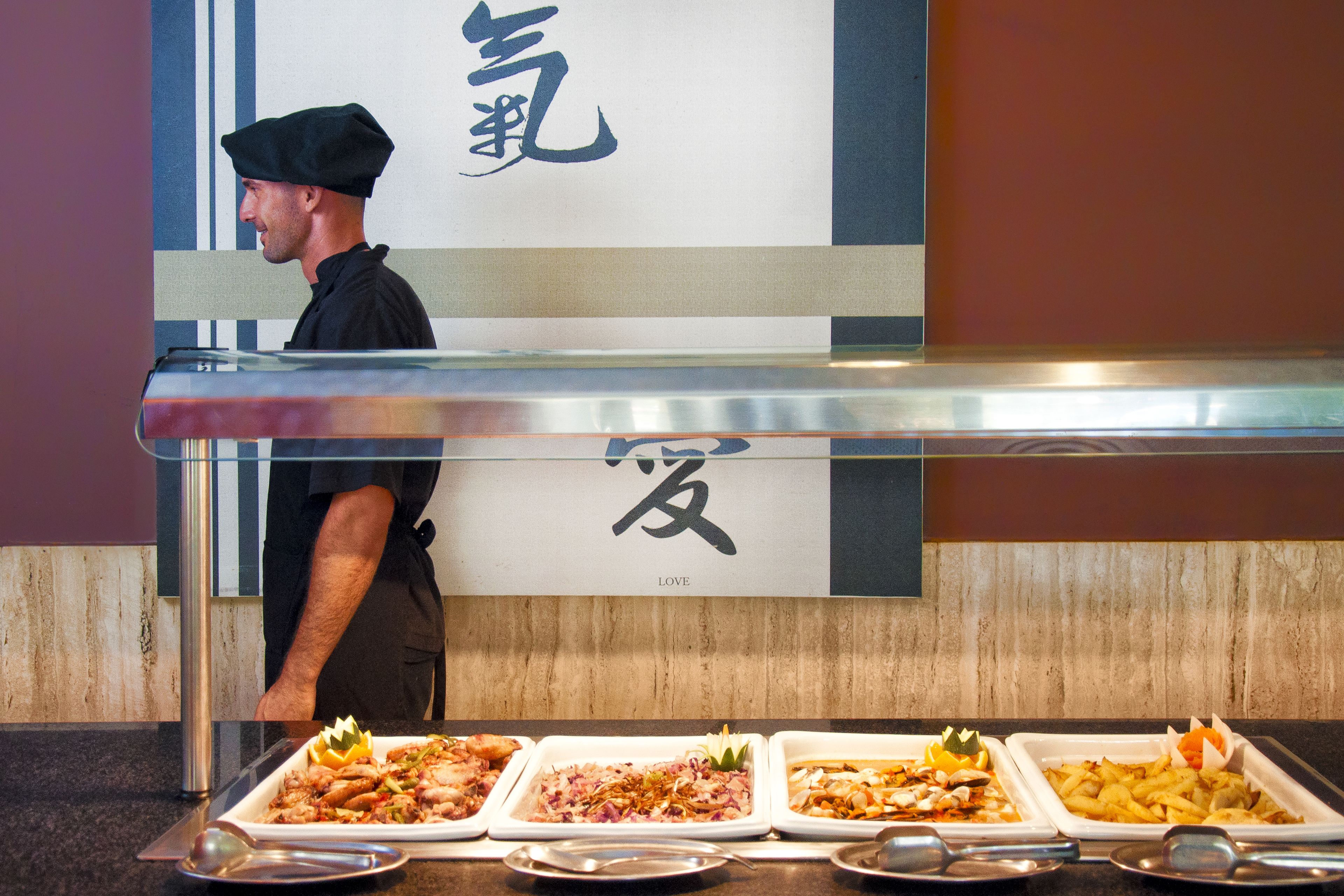 A buffet with various dishes, a chef in uniform, and a sign with Japanese characters.
