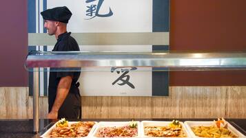 A buffet with various dishes, a chef in uniform, and a sign with Japanese characters.