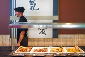 Een buffet met diverse gerechten, een kok in uniform en een bord met Japanse tekens.