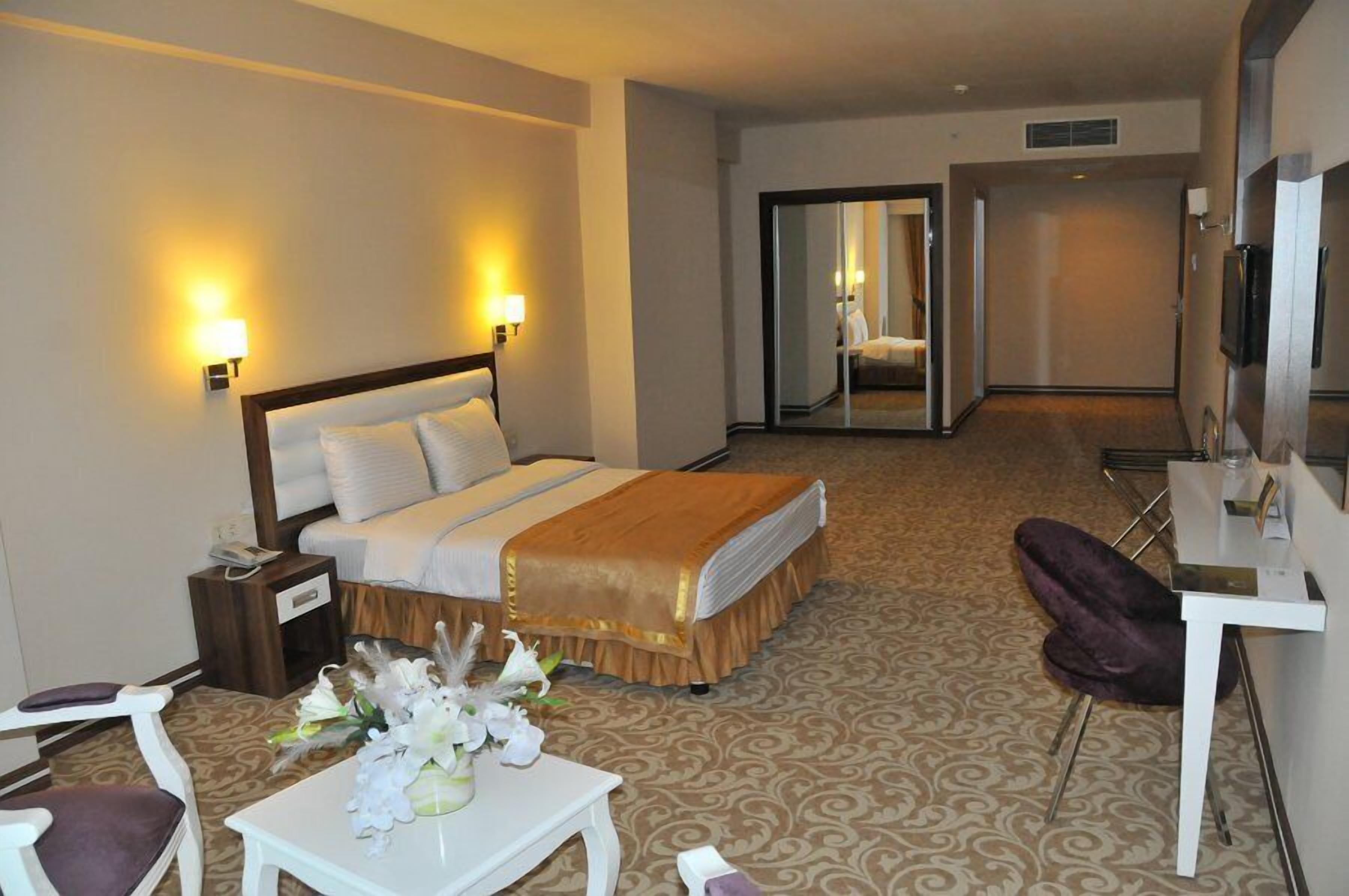 A hotel room with a bed, bedside table, lamp, chair, and a small table with flowers.
