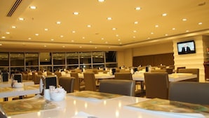 A spacious restaurant with multiple tables and chairs, recessed ceiling lights, and a television screen mounted on the wall. - Ozpark Hotel (Aksehir)