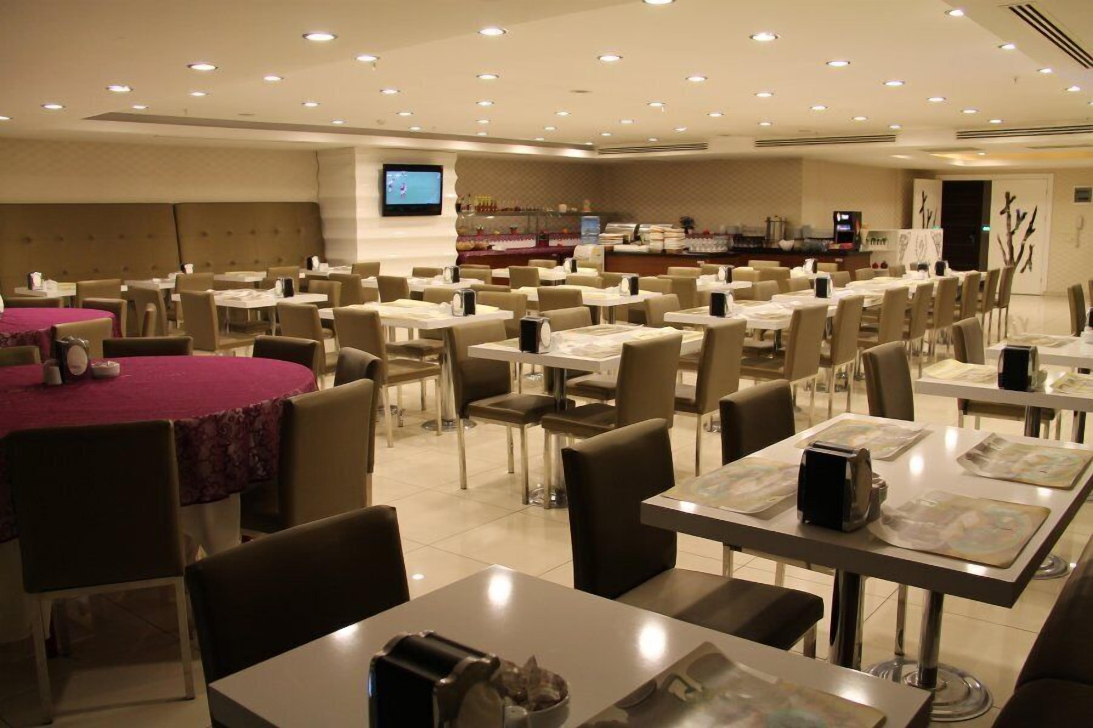 A large dining area with multiple tables and chairs, a buffet station, and a television screen on the wall.