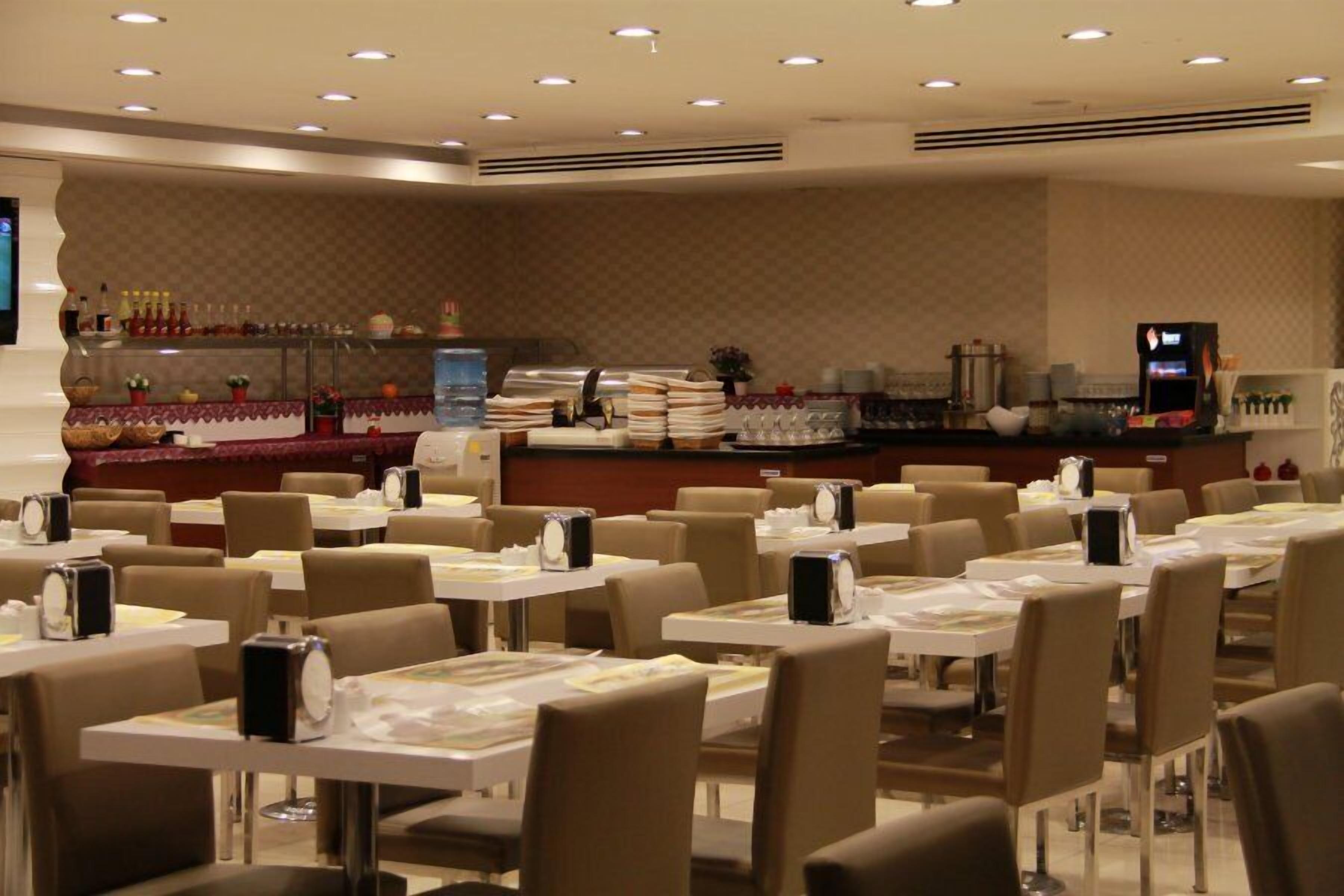 A restaurant with multiple tables and chairs, a counter with various items, and a television screen.