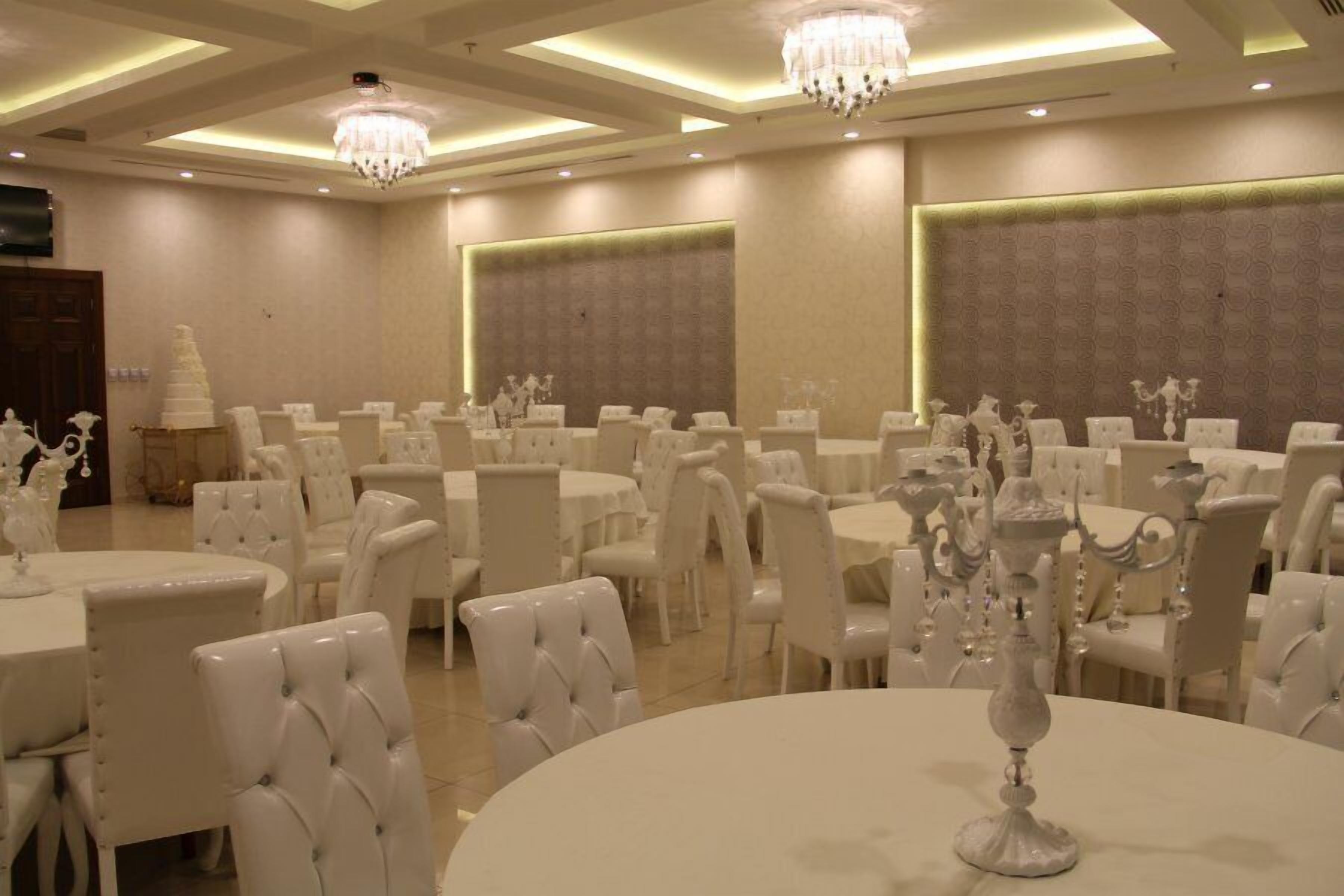A banquet hall with round tables and white chairs, chandeliers, and a large wall with a textured pattern.