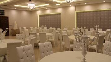 A banquet hall with round tables and white chairs, chandeliers, and a large wall with a textured pattern.