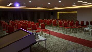 A conference room with rows of red chairs, a white table with a vase, and a patterned carpet.