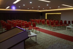 A conference room with rows of red chairs, a white table with a vase, and a patterned carpet.