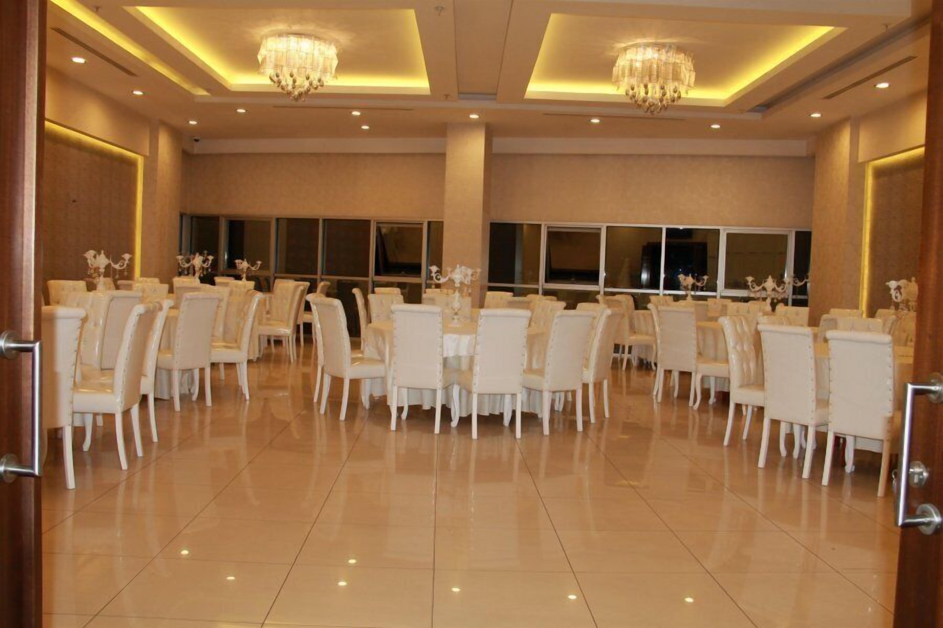 Une vaste salle de banquet avec des chaises blanches disposées en rangées, de grandes fenêtres et des lustres.
