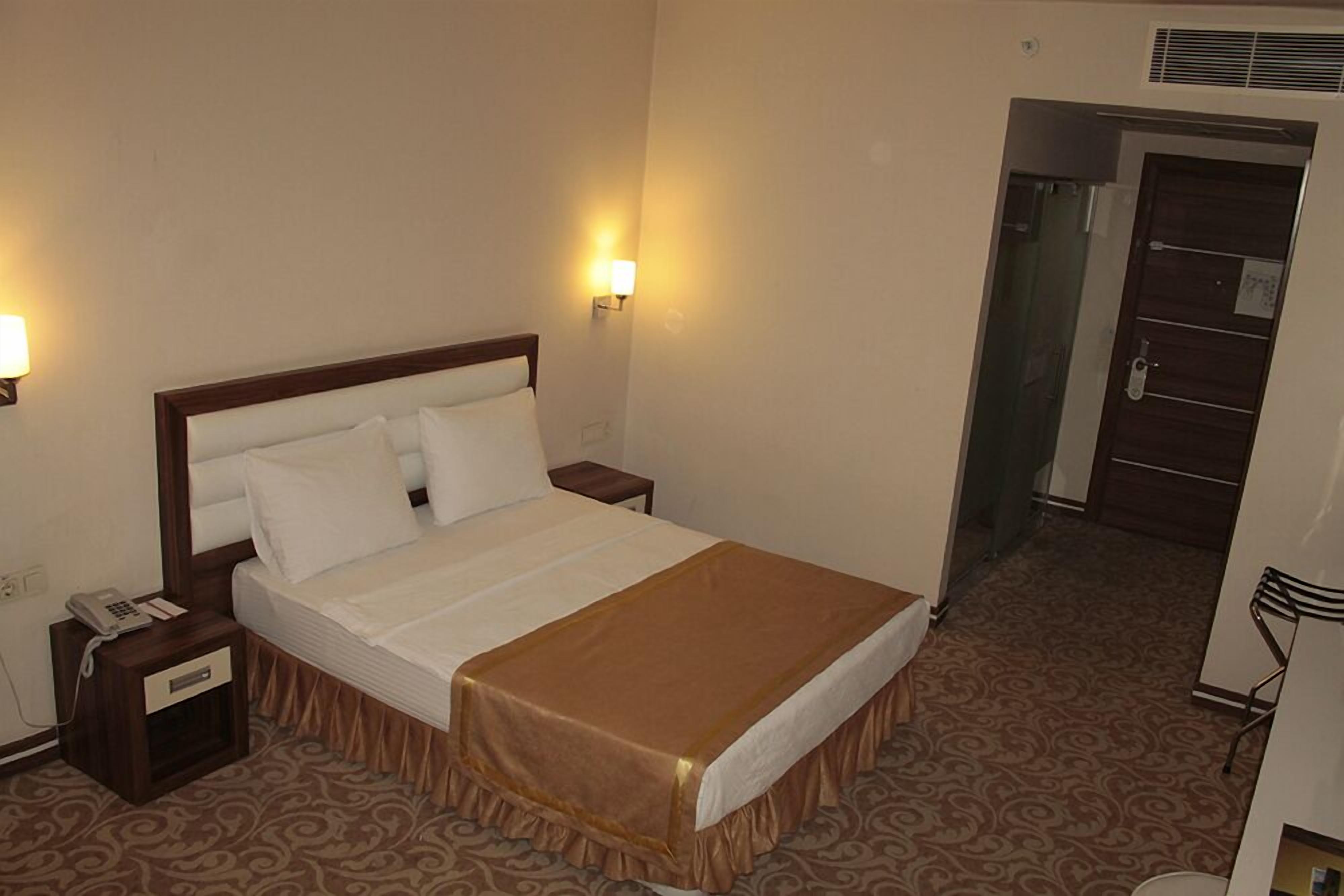Habitación de hotel con cama, lámparas de noche, teléfono y alfombra estampada.